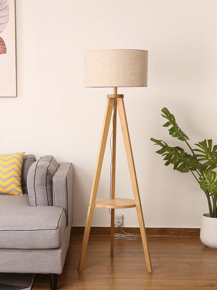 Wooden floor lamp in a living room setting with a sofa and plant.