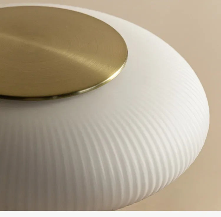 Round lamp with a gold top and white ribbed lampshade on a beige background