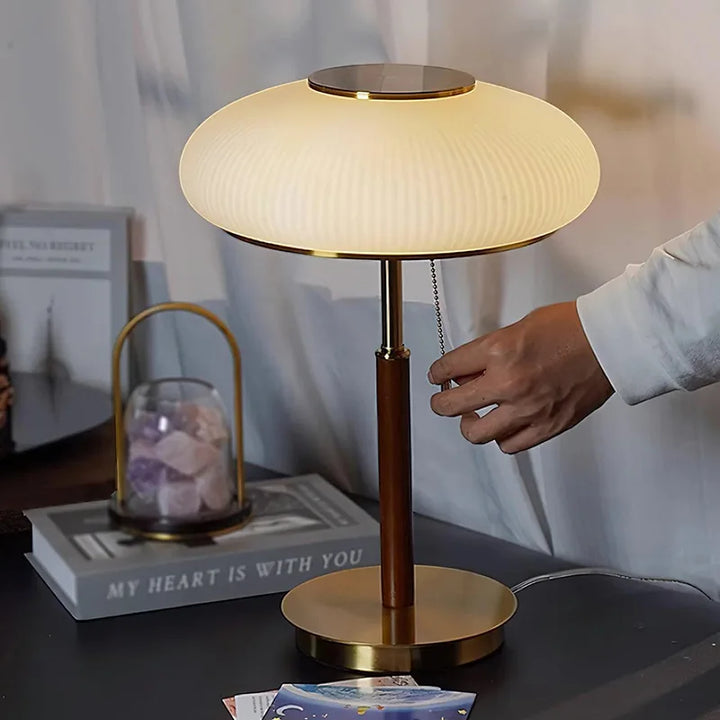 Person switching a table lamp on a desk with books and decor items in the background