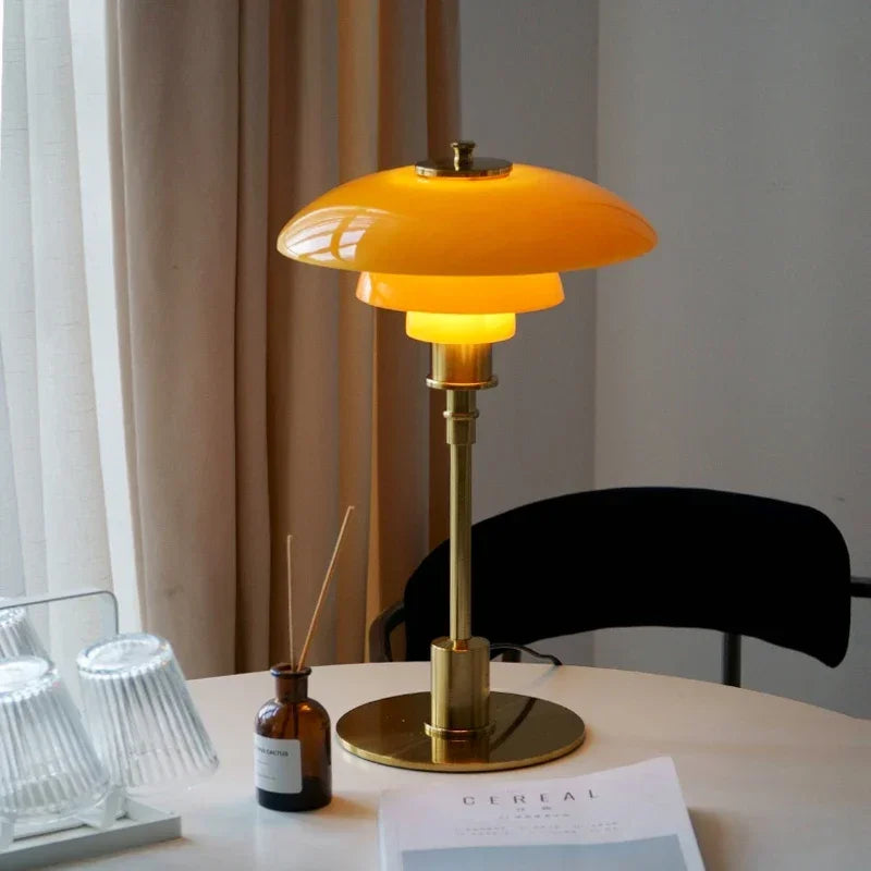 Table lamp with orange shade and gold base on a table with a magazine and bottles.