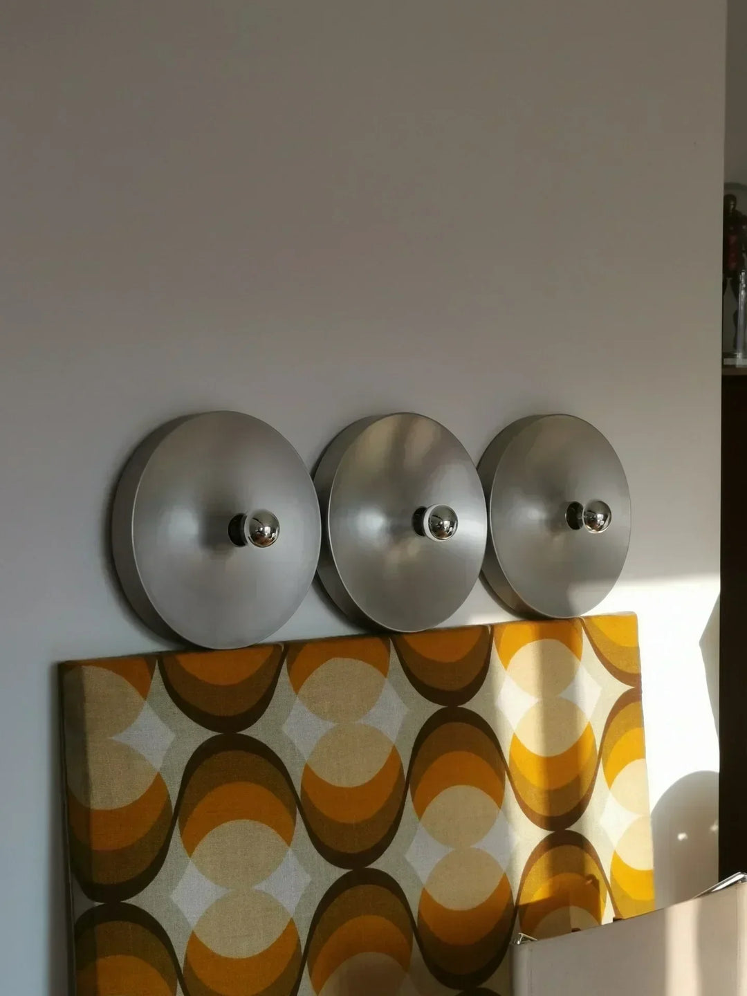 Three circular light fixtures on a white wall with a patterned fabric box below.