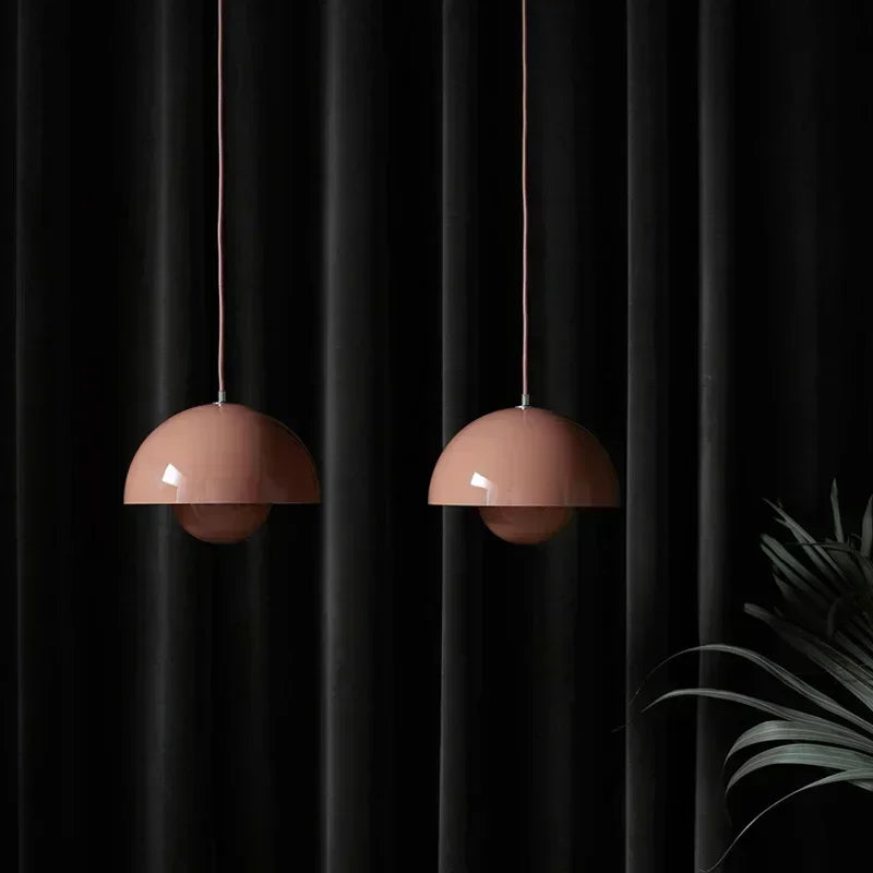 Two pink pendant lights hanging against a black curtain with a plant on the right.
