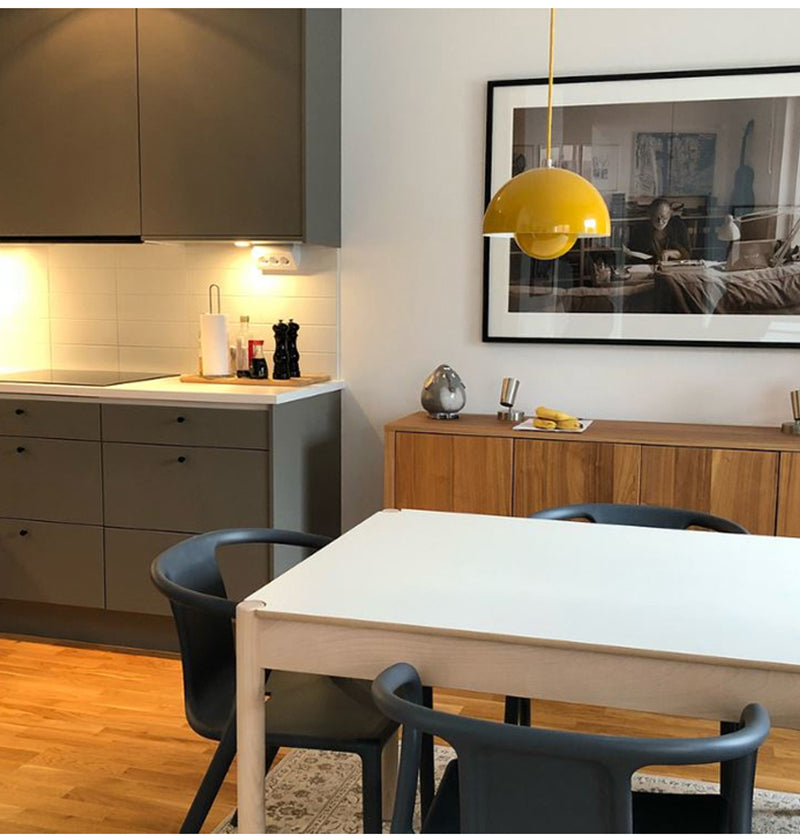 Modern kitchen with dining area featuring a yellow pendant light, wooden cabinets, and a white table.