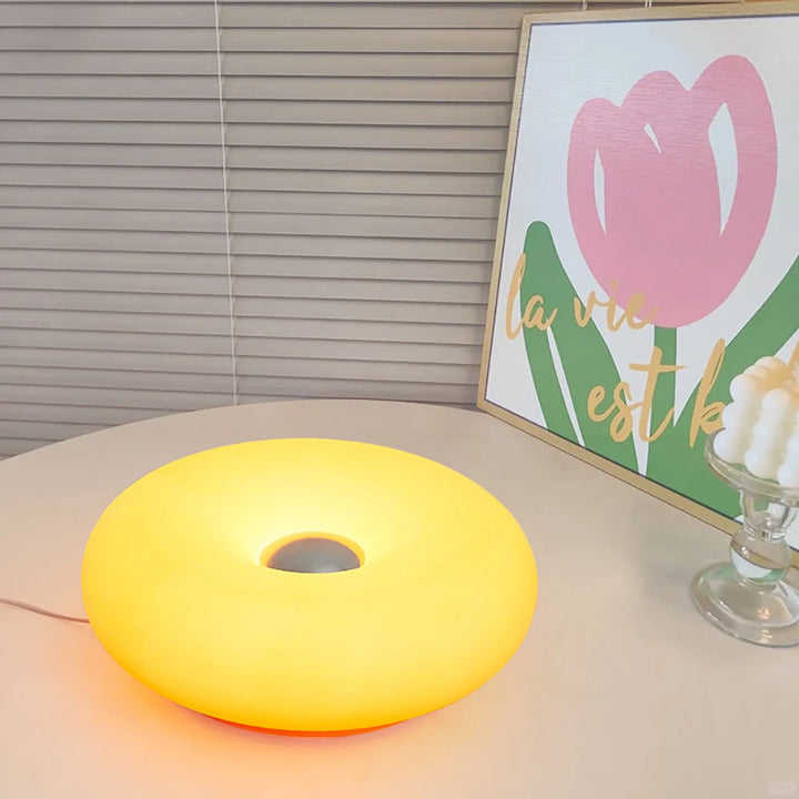 Yellow round lamp on a table with a framed picture of a pink tulip in the background