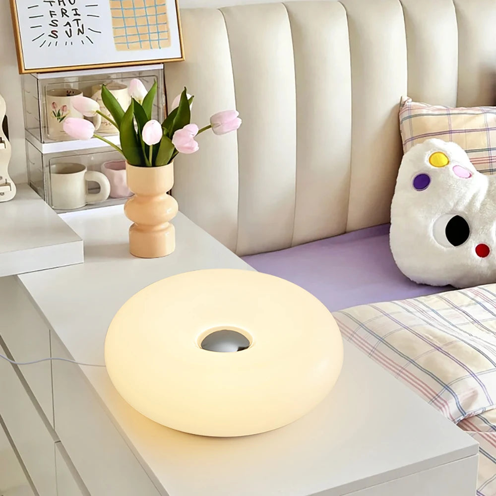 Round lamp on a coffee table with a vase of flowers and a couch in the background