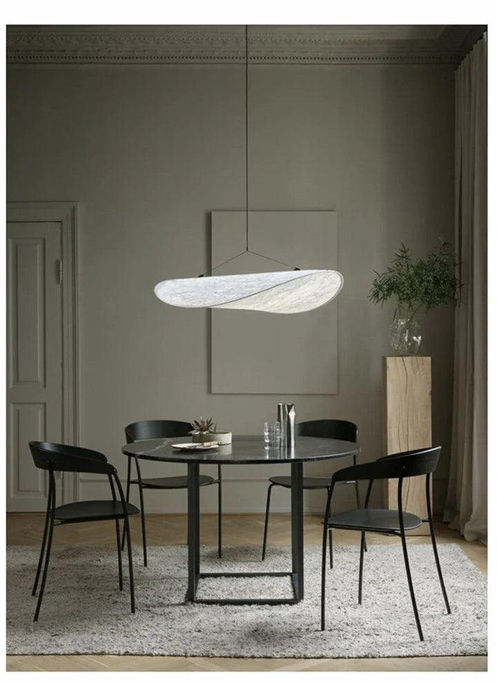 Modern dining room with a round glass table and black chairs, featuring a pendant light.