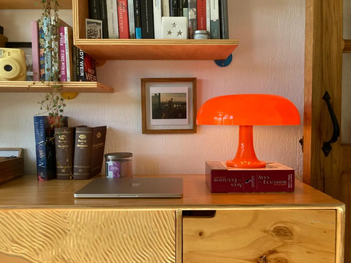 Wooden desk with orange lamp, books, and a laptop in a room setting.