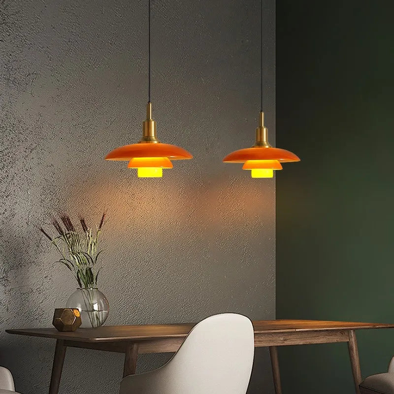 Two orange pendant lights hanging above a wooden table with a vase and decorative items.